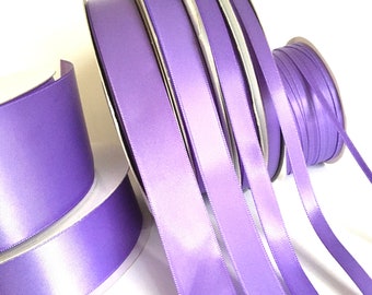 May include: Several spools of lavender satin ribbon are displayed against a white background. The ribbon is unwound from the spools, revealing its smooth, shiny texture. The image highlights the ribbon's color and sheen, perfect for crafts and decorations.
