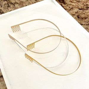 May include: Three gold hair combs with teeth on one end. The combs are arranged in a stack, with the largest comb at the bottom and the smallest comb at the top.