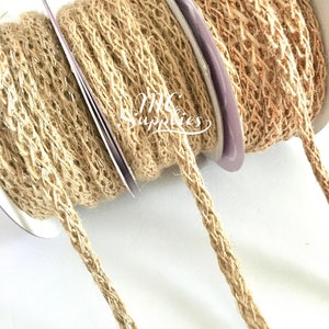 May include: Three spools of natural jute twine with a braided texture. The twine is wrapped around white spools with purple labels. The twine is unraveled and hanging down.