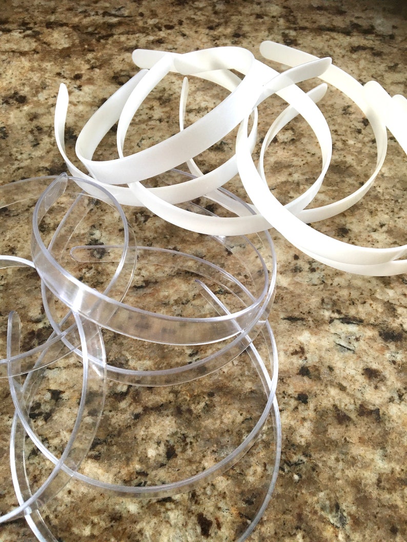 May include: A pile of white and clear plastic headbands. The white headbands are opaque and the clear headbands are translucent.