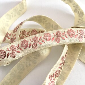 May include: Cream colored ribbon with a rose pattern in a metallic copper color. The ribbon is folded and twisted.