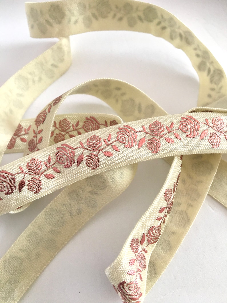 May include: Cream colored ribbon with a rose pattern in a metallic copper color. The ribbon is folded and twisted.
