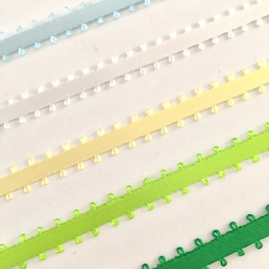 May include: Five different colors of ribbon with scalloped edges. The colors are light blue, white, yellow, light green, and green.