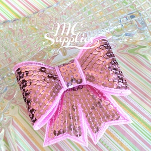 May include: A pink sequined bow with a light pink border. The bow is on a clear, textured surface with the text "MC Supplies" in white. The background is a striped pattern of pink, green, and white.