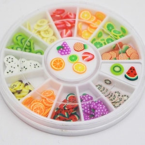 May include: A white plastic wheel with 12 compartments, each filled with colourful, miniature, 3D fruit slices. The fruit slices include watermelon, kiwi, pineapple, grapes, strawberries, oranges, lemons, and bananas.