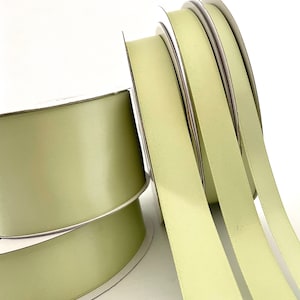 May include: Four spools of pale green satin ribbon. The ribbon is wound around white spools with silver trim.