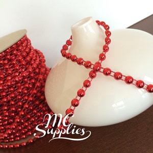 May include: A spool of red metallic bead garland. The garland is wrapped around a white ceramic vase. The text "MC Supplies" is visible in the image.
