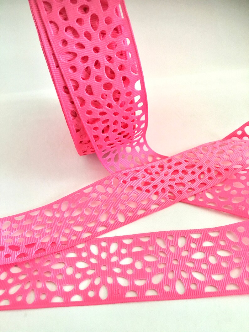 May include: Pink ribbon with a delicate, intricate cut-out pattern. The ribbon is made of a soft, silky material and has a subtle sheen.