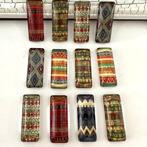 May include: Twelve rectangular glass tiles with different geometric patterns in shades of brown, red, green, blue, and white. The tiles have a glossy finish and are arranged in two rows of six.