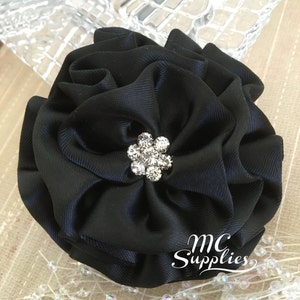 May include: A black satin flower with a rhinestone center. The flower is about 4 inches in diameter. The flower is on a white background with white beads.
