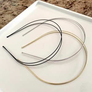 May include: Three metal headbands in different colors: gold, silver, and black. The headbands are lying on a white surface.