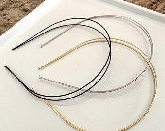 May include: Three metal headbands in different colors: gold, silver, and black. The headbands are lying on a white surface.