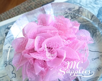 May include: A pink fabric flower with lace detailing, displayed on a clear acrylic surface. The flower is in a round shape and has a delicate, ruffled texture. The text "mc Supplies" is visible in the background.