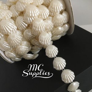 May include: A spool of white pearl-like shell trim. The trim is made of plastic and has a scalloped edge. The trim is on a white card with the text "MC Supplies" written in black.