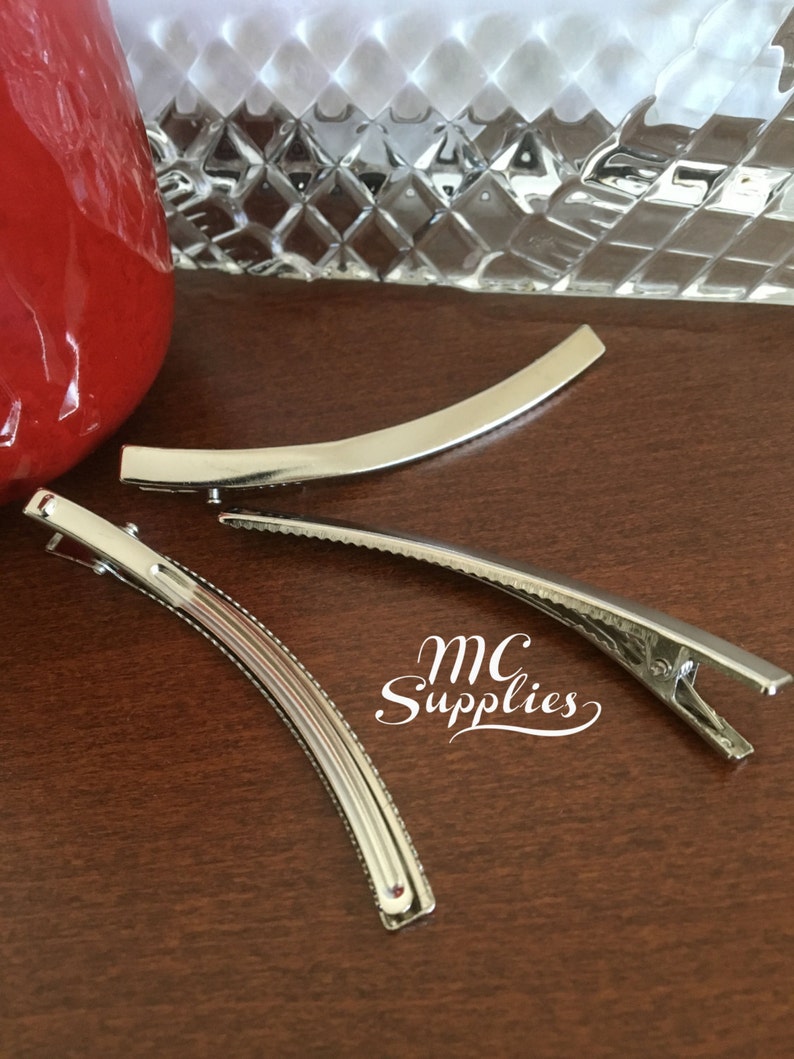 May include: Three silver metal hair clips. The clips are curved and have a ridged texture. The clips are on a wooden surface.