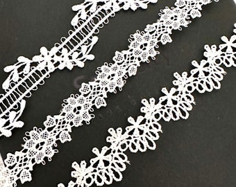 May include: Three white lace trims with different patterns and designs. The trims are arranged on a black surface.