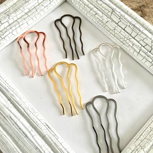 May include: Five hair combs in different colors: gold, silver, rose gold, black, and white. The combs are arranged in a row on a white surface.