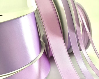 May include: A set of lavender satin ribbon spools. The ribbon is wound around white spools. The ribbon is smooth and shiny.