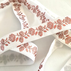 May include: White elastic ribbon with a rose pattern in a metallic copper color.