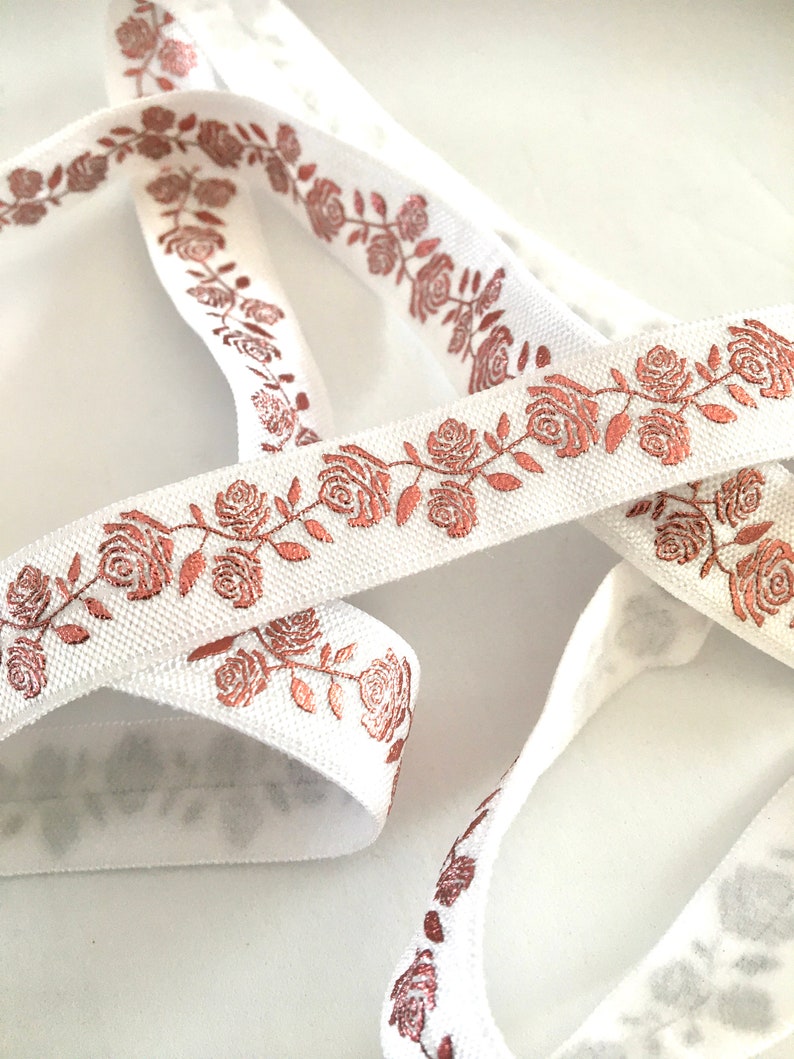May include: White elastic ribbon with a rose pattern in a metallic copper color.