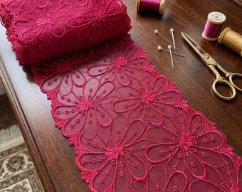 May include: A roll of deep pink floral lace trim featuring a repeating pattern of embroidered daisy-like flowers with scalloped edges. The lace is displayed alongside sewing supplies including spools of thread, straight pins, and metal scissors.