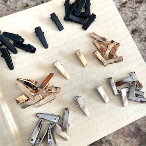 May include: Assortment of hair clips in black, gold, and silver. The clips are all the same size and shape, but they are made of different materials.