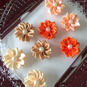 May include: Assortment of handmade fabric flower hair clips in peach, orange, and beige colors. Each flower has a pearl center and is attached to a metal alligator clip.