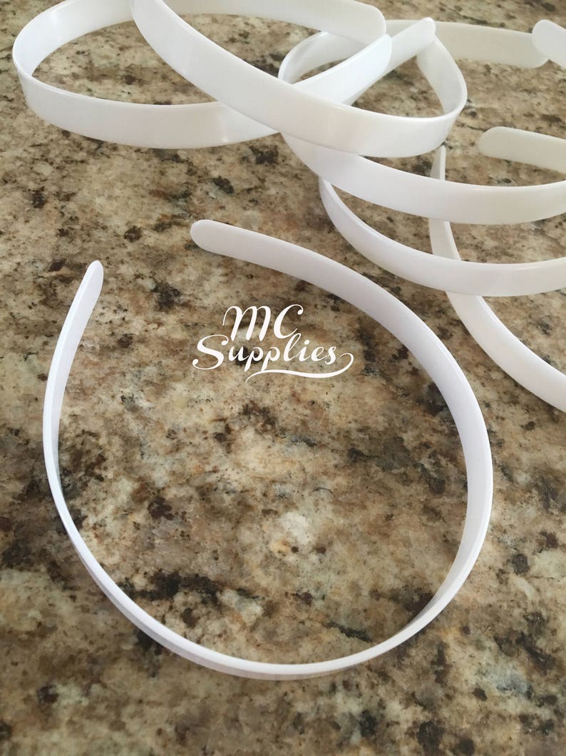 May include: A close-up of a pile of white plastic headband bases. The headbands are smooth and flexible. The text "MC Supplies" is visible in the image.