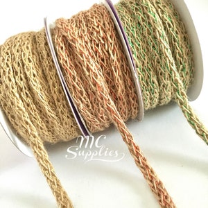 May include: Three spools of twine with a braided texture. The twine is natural brown with a thin strand of green, orange, or gold thread woven into the braid.