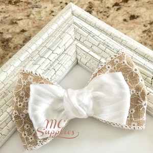 May include: A white bow with a burlap and lace trim. The bow is tied with a knot in the center. The bow is on a white background with the text "MC Supplies" in the lower left corner.