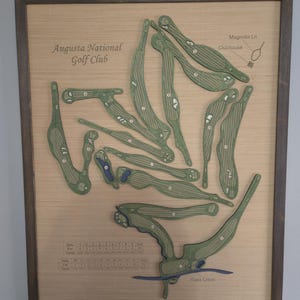 May include: Wooden framed map of Augusta National Golf Club. The map features green golf course layouts with white numbers, a blue creek, and the text "Augusta National Golf Club".