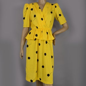 May include: A yellow dress with black polka dots and short sleeves. The dress features a V-neck, a peplum waist, and a knee-length skirt. The fabric has a subtle texture, and the polka dots are irregularly spaced.