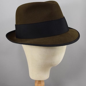 May include: A brown fedora hat with a black band. The hat is on a white mannequin head.