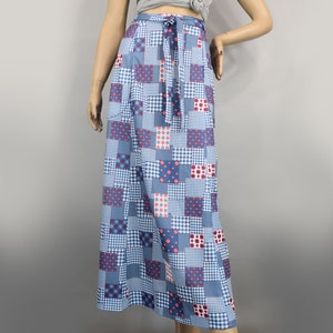May include: A long, patchwork skirt in shades of blue, white, and red. The skirt features a variety of square patterns, including gingham, polka dots, and solid colors. It has a tie-waist detail and is displayed on a mannequin.