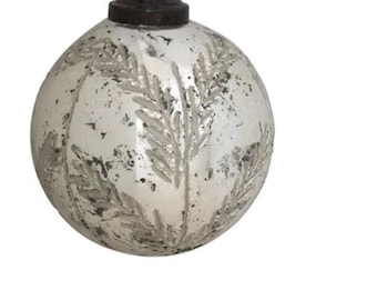 May include: A silver glass Christmas ornament with a white, leafy design. The ornament has a gold string for hanging.