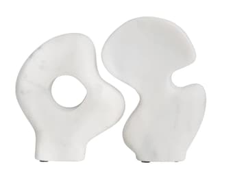 May include: Two white marble sculptures with abstract shapes. The sculptures are connected and have a hole in the center of one of the sculptures.