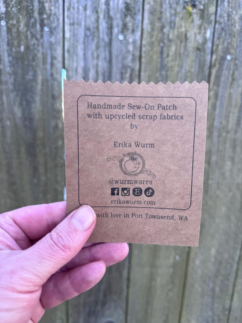 Puede incluir: Una etiqueta de papel marr&oacute;n con el texto "Handmade Sew-On Patch with upcycled scrap fabrics by Erika Wurm." La etiqueta tambi&eacute;n incluye iconos de redes sociales y el sitio web erikawurm.com.