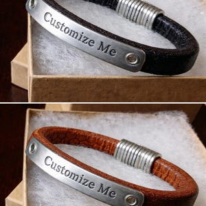 Può includere: Bracciale in pelle con una placca metallica con la scritta "Customize Me". Il bracciale è mostrato in due colori: nero e marrone. Il bracciale ha una chiusura color argento ed è presentato in una scatola di cartone.