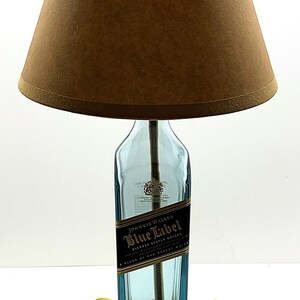 K&ouml;nnte beinhalten: Eine einzigartige Tischlampe aus einer recycelten Johnnie Walker Blue Label Whiskyflasche. Die Lampe hat einen braunen Lampenschirm und steht auf einem dunklen Holzsockel. Das Etikett der Flasche ist sichtbar.