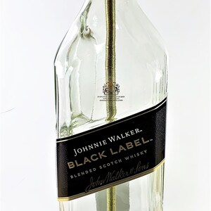 May include: A clear glass bottle lamp with a gold metal top and a brown wooden base. The bottle is labeled "Johnnie Walker Black Label Blended Scotch Whisky" and "Aged 12 Years".