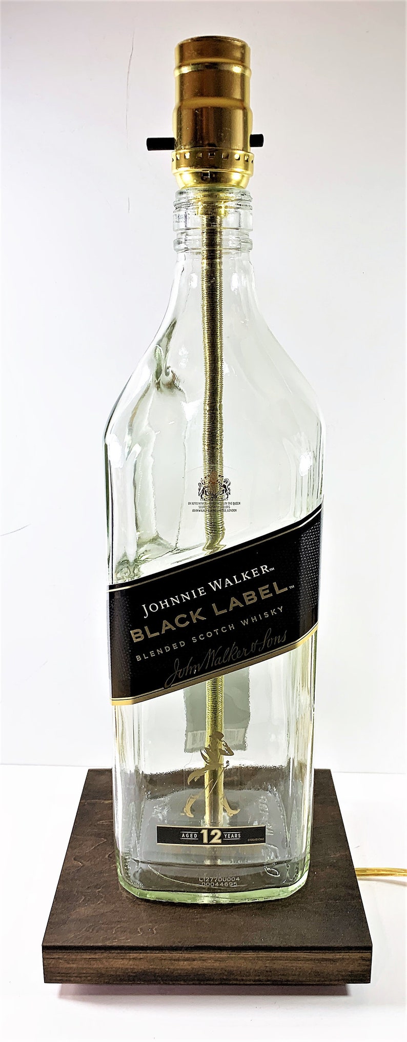 May include: A clear glass bottle lamp with a gold metal top and a brown wooden base. The bottle is labeled "Johnnie Walker Black Label Blended Scotch Whisky" and "Aged 12 Years".