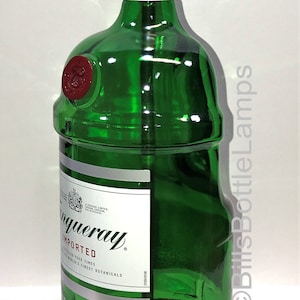 Puede incluir: Una botella de vidrio verde con una pantalla de l&aacute;mpara dorada en la parte superior. La botella est&aacute; etiquetada como "Tanqueray Imported London Dry Gin" y tiene un sello de cera rojo. La botella est&aacute; sentada sobre una base de madera.