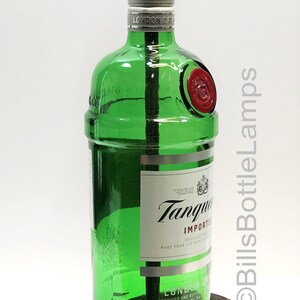 May include: A green glass bottle lamp with a wooden base. The bottle is labeled "Tanqueray Imported London Dry Gin" and has a red seal. The lamp has a gold light socket and a black switch.