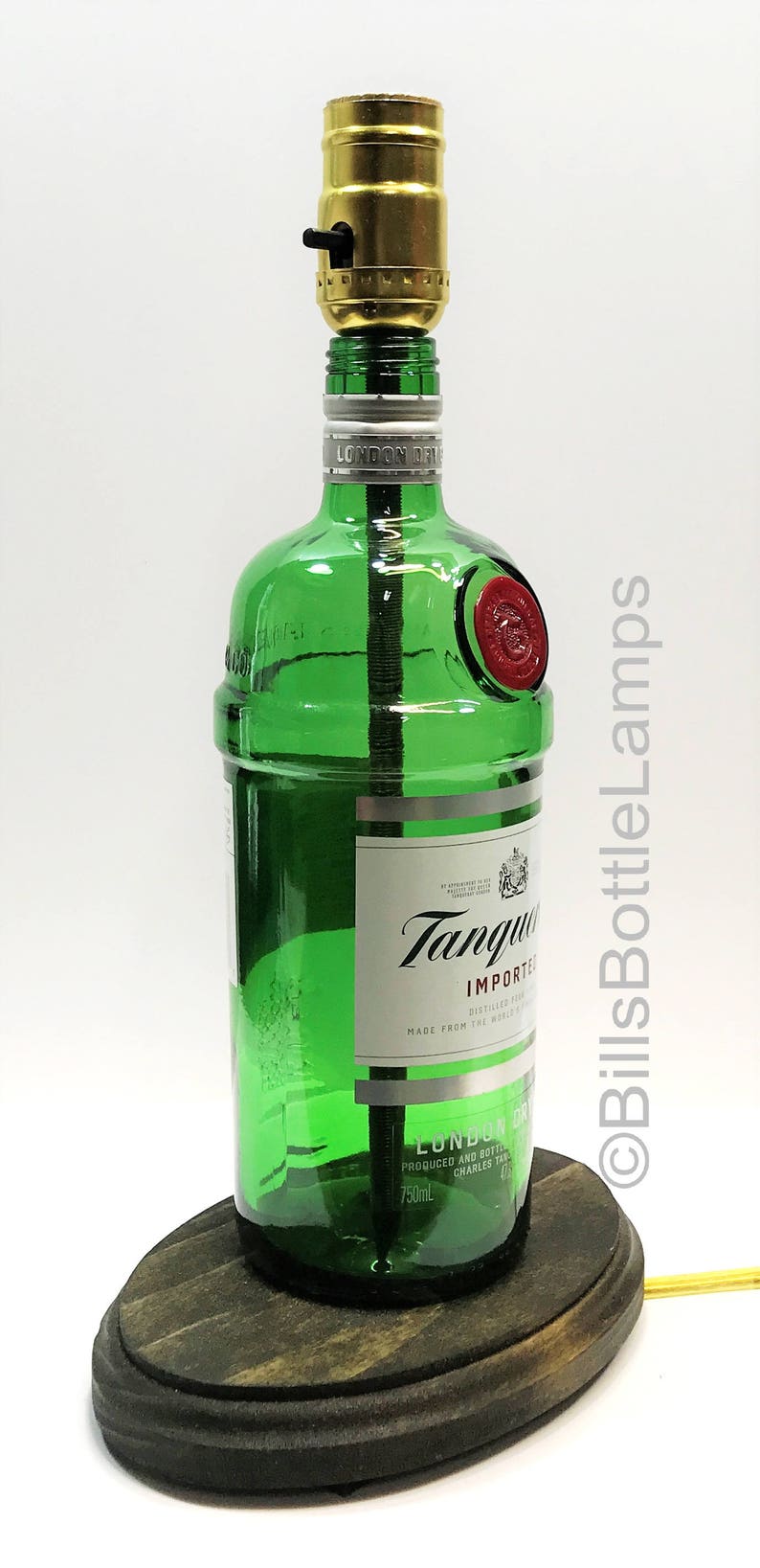 May include: A green glass bottle lamp with a wooden base. The bottle is labeled "Tanqueray Imported London Dry Gin" and has a red seal. The lamp has a gold light socket and a black switch.