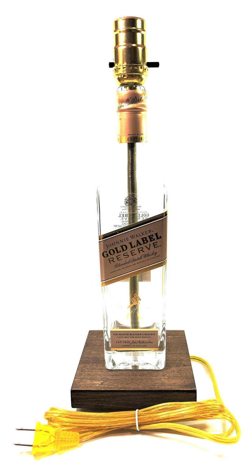 May include: A table lamp made from a repurposed Johnnie Walker Gold Label Reserve bottle. The lamp has a gold-colored socket and a brown wooden base. The bottle label reads "Johnnie Walker Gold Label Reserve Blended Scotch Whisky".