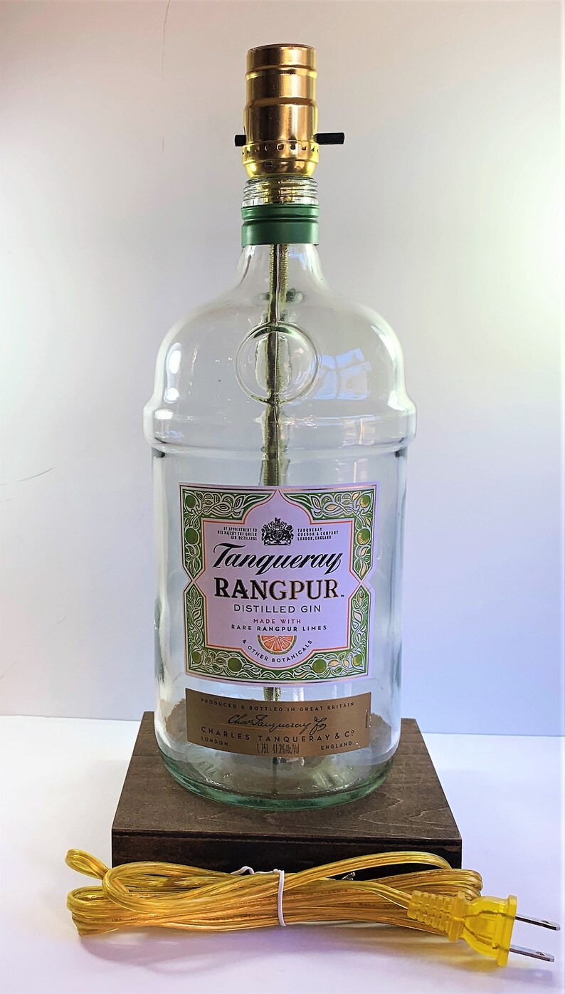 May include: A clear glass bottle lamp with a gold colored lampshade and a green base. The bottle is labeled "Tanqueray Rangpur. Distilled Gin. Made with Rare Rangpur Limes & Other Botanicals. Produced & Bottled in Great Britain. Charles Tanqueray & Co. London England."