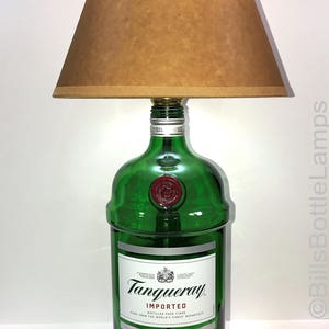 Puede incluir: Una l&aacute;mpara de botella de vidrio verde con una pantalla marr&oacute;n. La botella est&aacute; etiquetada con "Tanqueray Imported London Dry Gin".