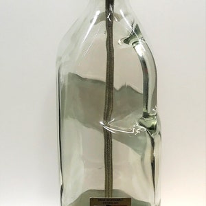 Puede incluir: Una l&aacute;mpara de botella de vidrio transparente con una pantalla de metal dorado y una base de madera. La botella tiene una etiqueta que dice "Drink Responsibly" y "Diageo".