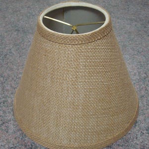 May include: A brown burlap lampshade with a wire frame. The lampshade is cone-shaped and has a simple design.