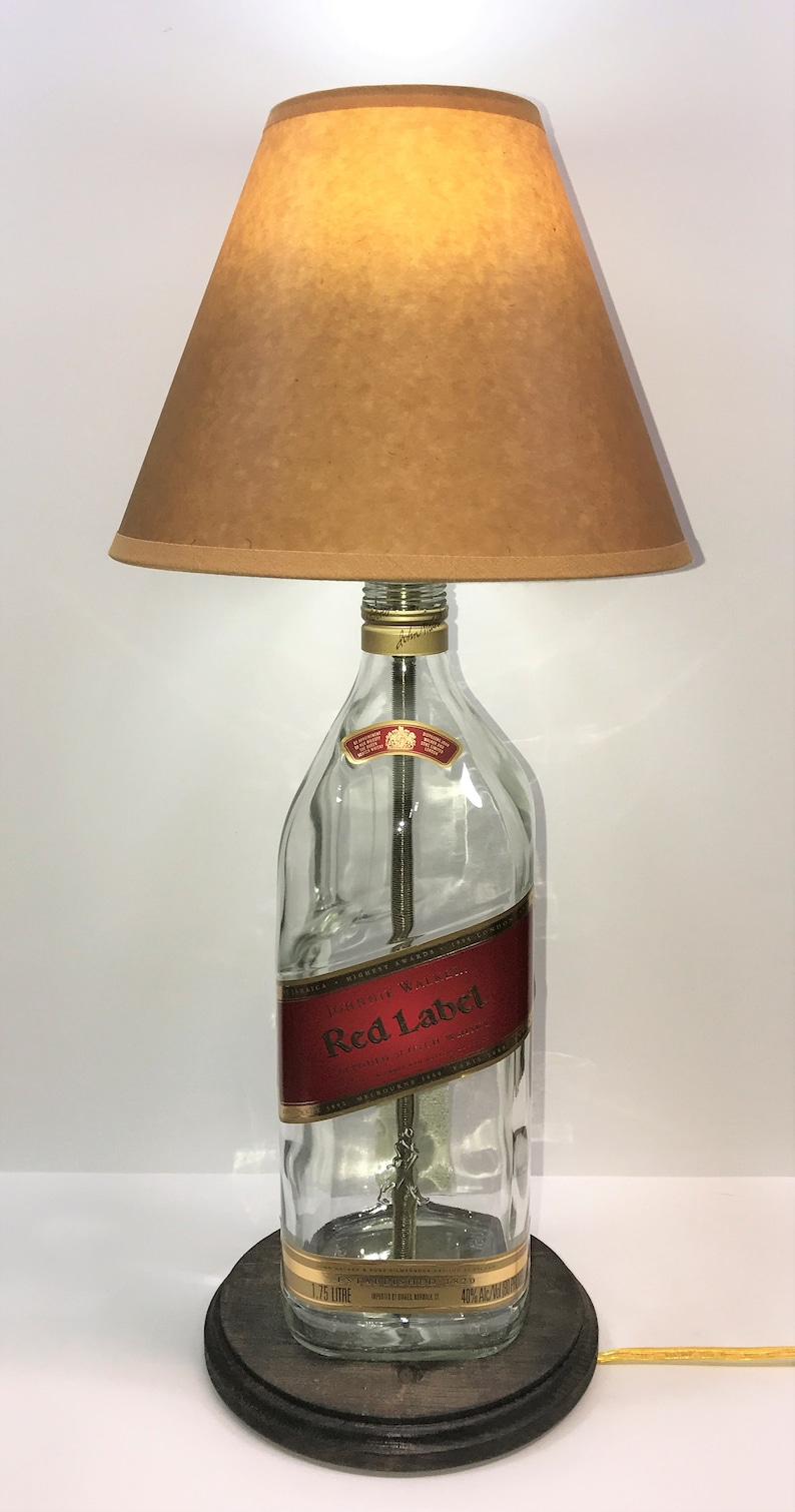 Puede incluir: Una l&aacute;mpara de mesa hecha con una botella de whisky Johnnie Walker Red Label reutilizada con una pantalla marr&oacute;n. La botella es de vidrio transparente con una etiqueta dorada y una base de madera.